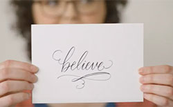 Woman holding up a card that says believe on it